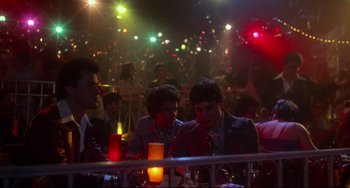 Movie still from “Saturday Night Fever” (1977), directed by John Badham – A group of people sitting at a table in a room; Wide shot, Over the shoulder angle