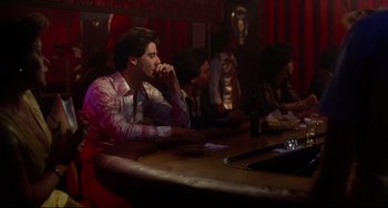 Movie still from “Saturday Night Fever” (1977), directed by John Badham – A man sitting at a table in front of a bottle of beer; Wide shot, Over the shoulder angle