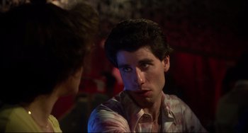 Movie still from “Saturday Night Fever” (1977), directed by John Badham – A young man with a serious look on his face; Close Up shot, Over the shoulder angle