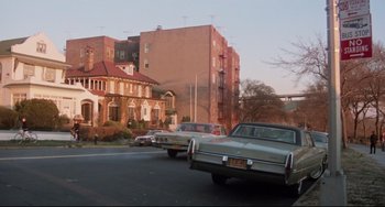 Movie still from “Saturday Night Fever” (1977), directed by John Badham – Cars driving down a street near a tall building; Extreme Wide shot, Low angle