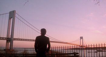Movie still from “Saturday Night Fever” (1977), directed by John Badham – A man standing in front of a bridge with a sunset in the background; Extreme Wide shot, Low angle