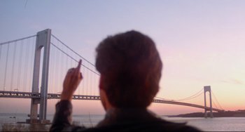 Movie still from “Saturday Night Fever” (1977), directed by John Badham – A man pointing to a bridge that is over a body of water; Medium shot, Over the shoulder angle