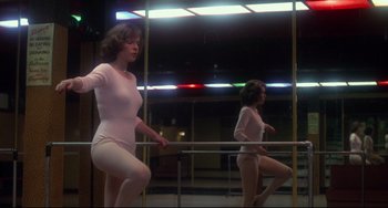 Movie still from “Saturday Night Fever” (1977), directed by John Badham – A woman in a white leotard is standing in front of a mirror; Wide shot, Low angle