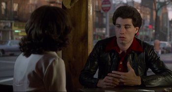 Movie still from “Saturday Night Fever” (1977), directed by John Badham – A man and a woman are sitting at a table talking; Medium shot, Over the shoulder angle
