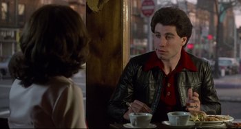 Movie still from “Saturday Night Fever” (1977), directed by John Badham – A man and a woman sitting in front of each other at a table; Medium shot, Over the shoulder angle