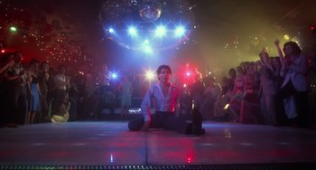 Movie still from “Saturday Night Fever” (1977), directed by John Badham – A man sitting on the floor in front of a crowd; Wide shot, Low angle