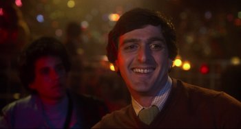 Movie still from “Saturday Night Fever” (1977), directed by John Badham – A young man smiling at the camera in a dark room; Close Up shot, Low angle