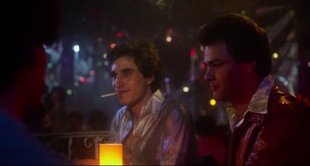 Movie still from “Saturday Night Fever” (1977), directed by John Badham – Two young men sitting at a table in front of a candle; Medium shot, Over the shoulder angle