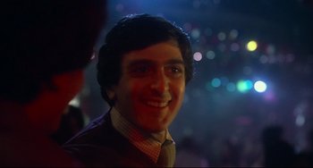 Movie still from “Saturday Night Fever” (1977), directed by John Badham – A person wearing a suit and smiling; Close Up shot, Low angle