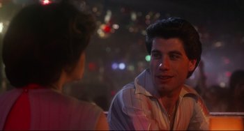 Movie still from “Saturday Night Fever” (1977), directed by John Badham – A man and a woman sitting at a table in front of lights; Close Up shot, Over the shoulder angle