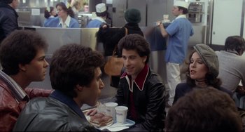 Movie still from “Saturday Night Fever” (1977), directed by John Badham – A group of men sitting at a table eating food; Medium shot, Over the shoulder angle