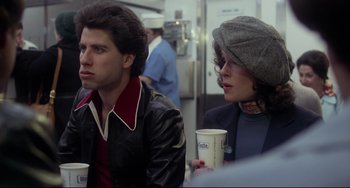 Movie still from “Saturday Night Fever” (1977), directed by John Badham – A man and a woman sitting next to each other holding drinks; Medium shot, Over the shoulder angle