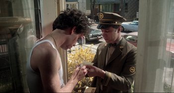 Movie still from “Saturday Night Fever” (1977), directed by John Badham – A man in a military uniform and a man in a white tank top; Medium shot, Low angle