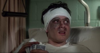 Movie still from “Saturday Night Fever” (1977), directed by John Badham – A man with bandages on his head holding cards; Close Up shot, High angle