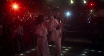 Movie still from “Saturday Night Fever” (1977), directed by John Badham – A man and a woman are dancing on a dance floor in front of a crowd of onlookers; Wide shot, Low angle