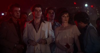 Movie still from “Saturday Night Fever” (1977), directed by John Badham – A group of people standing in a dark room; Medium shot, Low angle