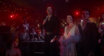 Movie still from “Saturday Night Fever” (1977), directed by John Badham – A man and a woman are standing in front of a crowd; Medium shot, Low angle