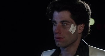 Movie still from “Saturday Night Fever” (1977), directed by John Badham – A man with bandaids on his face; Close Up shot, Over the shoulder angle