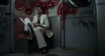 Movie still from “Saturday Night Fever” (1977), directed by John Badham – A man sitting on a bench smoking a cigarette; Wide shot, Low angle