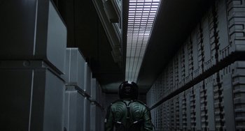 Movie still from “Saturn 3” (1980), directed by John Barry – A man in a green jacket walking down a hallway; Wide shot, Overhead angle