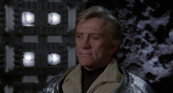 Movie still from “Saturn 3” (1980), directed by John Barry – An older man wearing a jacket and standing in front of a building; Close Up shot, Over the shoulder angle