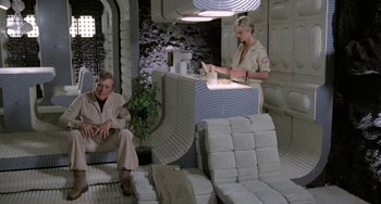 Movie still from “Saturn 3” (1980), directed by John Barry – A man and a woman sitting in a room with a bunch of towels; Wide shot, High angle