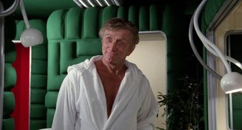 Movie still from “Saturn 3” (1980), directed by John Barry – A man in a white bathrobe standing next to a green wall; Medium shot, Low angle