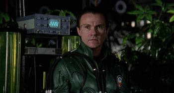 Movie still from “Saturn 3” (1980), directed by John Barry – A man in a green jacket standing in front of plants; Close Up shot, Over the shoulder angle