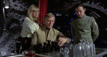 Movie still from “Saturn 3” (1980), directed by John Barry – A group of people standing next to each other in a room; Medium shot, Over the shoulder angle