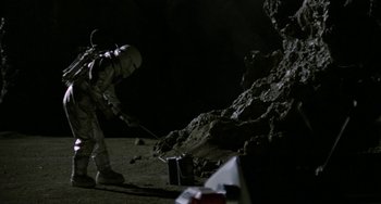 Movie still from “Saturn 3” (1980), directed by John Barry – A person in a spacesuit is standing next to rocks; Wide shot, Overhead angle
