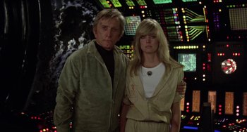 Movie still from “Saturn 3” (1980), directed by John Barry – A man standing next to a woman in front of a screen; Medium shot, Low angle