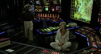 Movie still from “Saturn 3” (1980), directed by John Barry – A woman sitting on the ground in a room; Wide shot, High angle