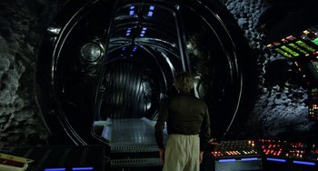 Movie still from “Saturn 3” (1980), directed by John Barry – A man standing in front of a large metal object; Wide shot, Over the shoulder angle
