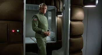 Movie still from “Saturn 3” (1980), directed by John Barry – A man standing in a room holding a cell phone; Medium shot, Low angle