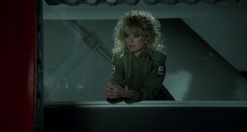 Movie still from “Saturn 3” (1980), directed by John Barry – A woman with blonde curly hair sitting on a ledge; Medium shot, Over the shoulder angle