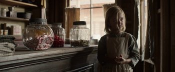Movie still from “Godless” (2017), directed by Scott Frank – A little girl standing in front of a counter with jars; Medium shot, Over the shoulder angle