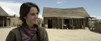 Movie still from “Godless” (2017), directed by Scott Frank – A woman standing in front of an old barn; Close Up shot, Over the shoulder angle