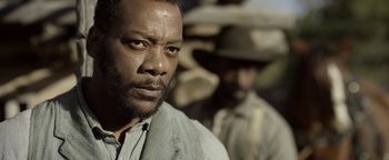 Movie still from “Godless” (2017), directed by Scott Frank – A man with a beard is looking at the camera while another man stands in the background; Close Up shot, Over the shoulder angle
