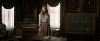 Movie still from “Godless” (2017), directed by Scott Frank – A woman standing in front of a window in a room; Medium shot, Low angle