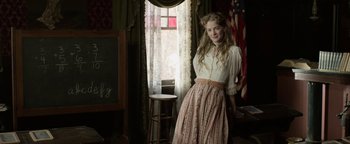 Movie still from “Godless” (2017), directed by Scott Frank – A woman in a dress standing in front of a window; Medium shot, Low angle