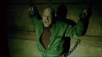 Movie still from “Saw 3D” (2010), directed by Kevin Greutert – A man in a green jacket holding a metal chain; Medium shot, Low angle