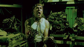 Movie still from “Saw 3D” (2010), directed by Kevin Greutert – A man in chains is standing in front of a machine; Medium shot, High angle