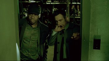 Movie still from “Saw 3D” (2010), directed by Kevin Greutert – Two men standing next to each other in a dark room; Medium shot, Low angle