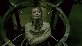 Movie still from “Saw 3D” (2010), directed by Kevin Greutert – A woman with a neck brace sitting in a cage; Medium shot, High angle