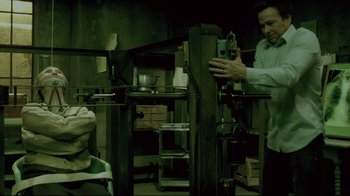 Movie still from “Saw 3D” (2010), directed by Kevin Greutert – A man standing in front of a machine in a room; Medium shot, High angle
