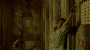 Movie still from “Saw 3D” (2010), directed by Kevin Greutert – A man leaning up against a wall with his arm raised; Medium shot, Low angle
