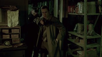Movie still from “Saw 3D” (2010), directed by Kevin Greutert – A man in a trench coat and tie holding a gun in front of another man; Medium shot, Over the shoulder angle