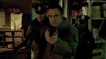 Movie still from “Saw 3D” (2010), directed by Kevin Greutert – A man holding a gun while standing next to another man; Medium shot, Over the shoulder angle