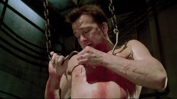 Movie still from “Saw 3D” (2010), directed by Kevin Greutert – A man with blood on his body and chest is holding a pair of metal hooks; Close Up shot, High angle