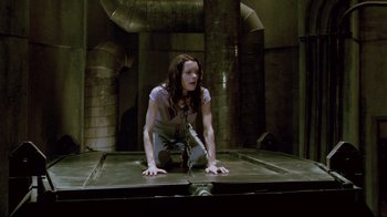 Movie still from “Saw 3D” (2010), directed by Kevin Greutert – A woman is crouched down on a metal platform; Wide shot, High angle